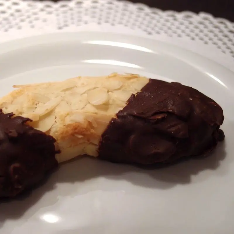 Galleta de almendra laminada con extremos bañados en chocolate sobre un plato blanco