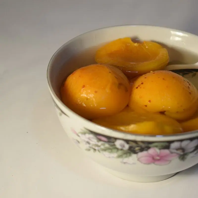 Cuenco de porcelana con albaricoques en almíbar y una cuchara