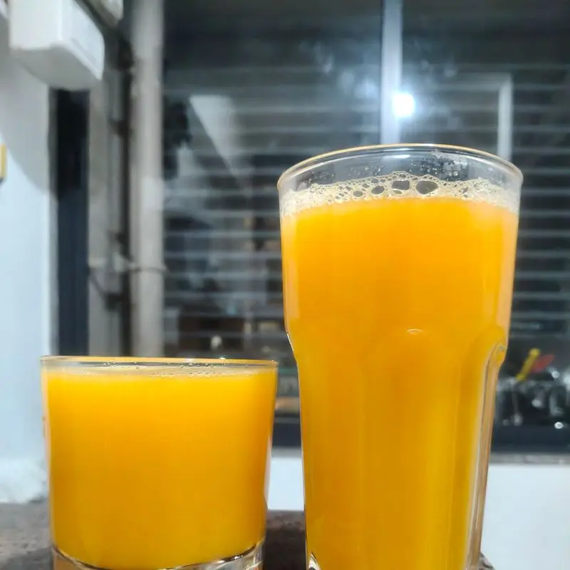 Dos vasos con zumo de color naranja intenso sobre una encimera junto a una ventana