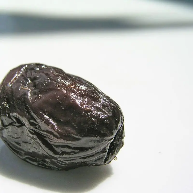 Una aceituna negra arrugada sobre una superficie blanca