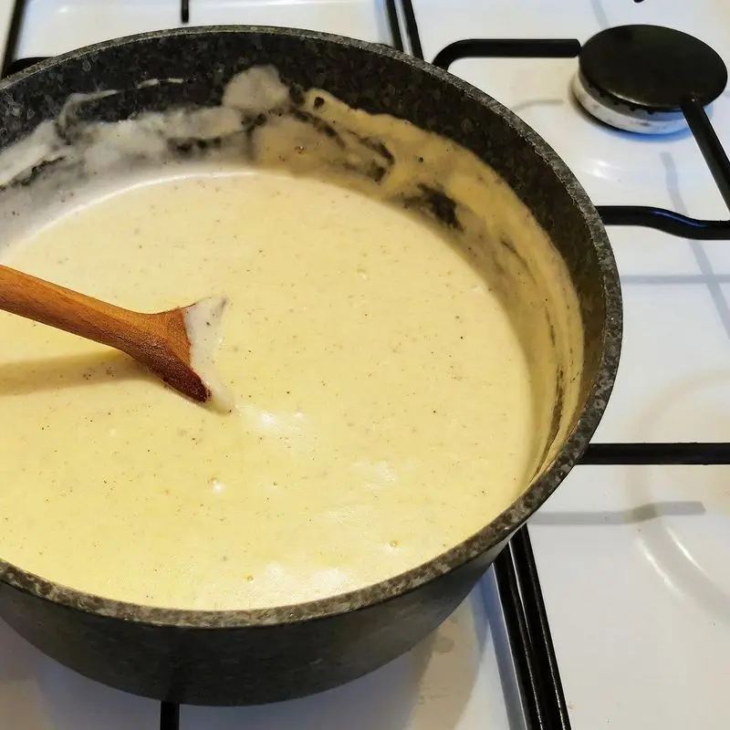 Salsa bechamel cremosa en un cazo con cuchara de madera