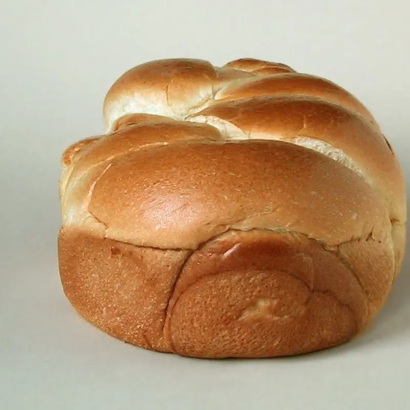 Pan brioche dorado en forma de hogaza trenzada sobre fondo claro