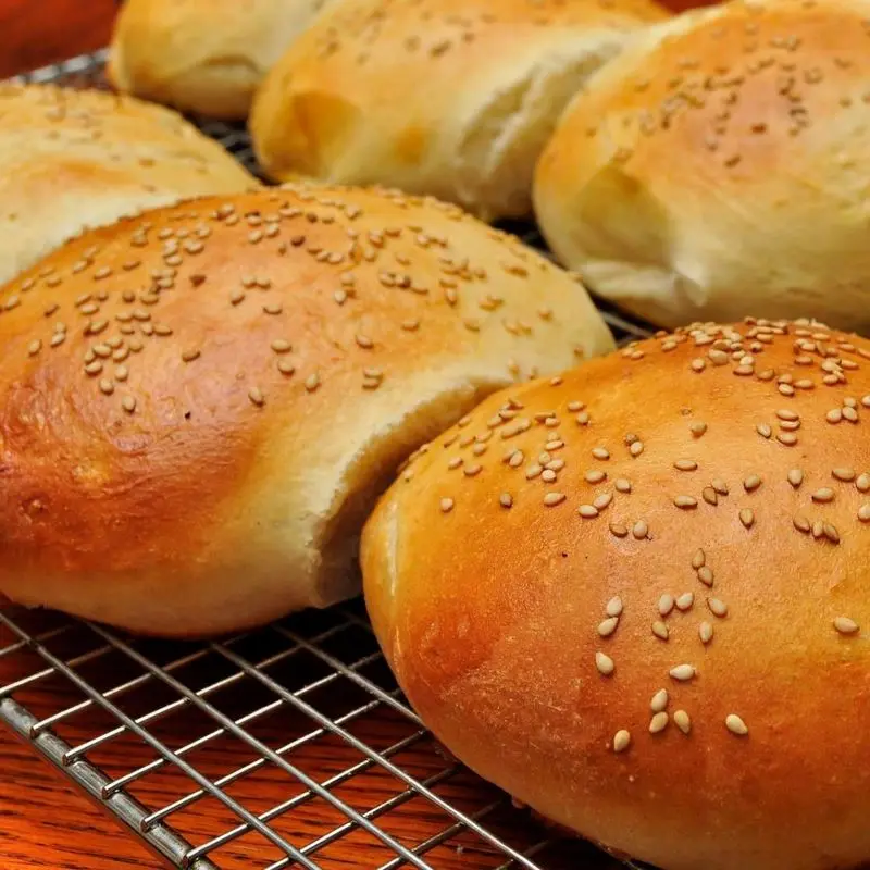 Panes de hamburguesa con sésamo recién horneados sobre una rejilla de enfriar