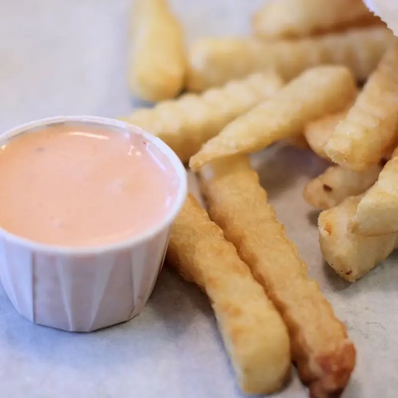 Vasito de papel con salsa rosada cremosa junto a patatas fritas