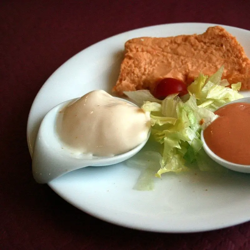 Porción de pastel de cabracho en un plato blanco con dos salsas y lechuga