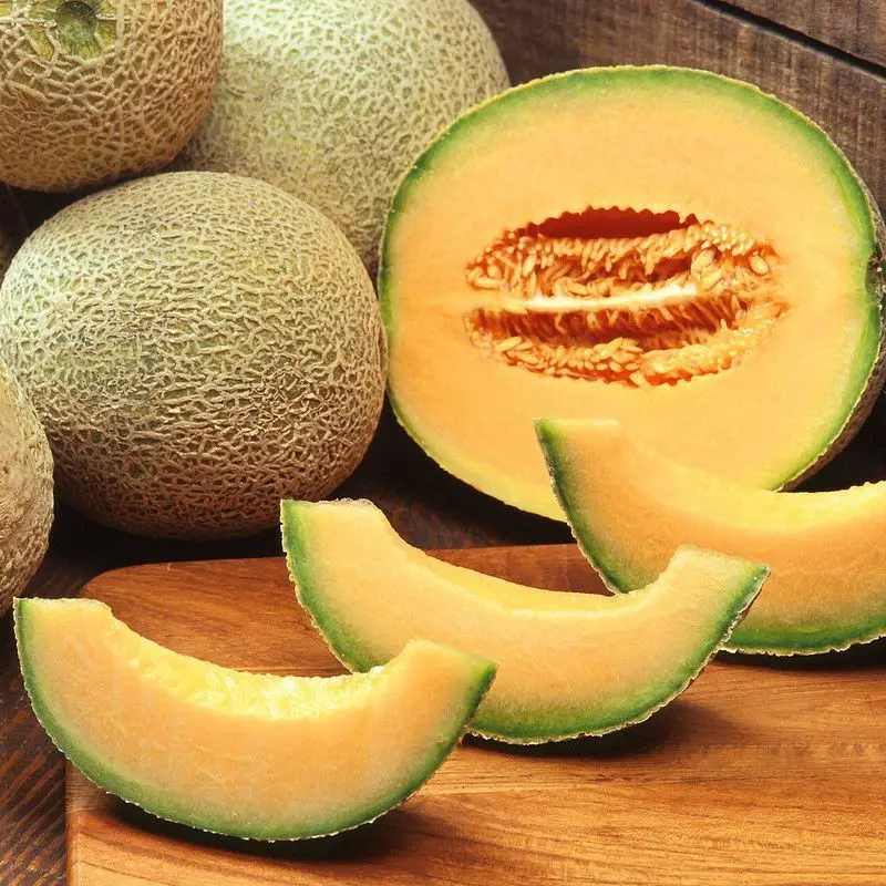 Melones cantalupo enteros y gajos de melón sobre una tabla de madera