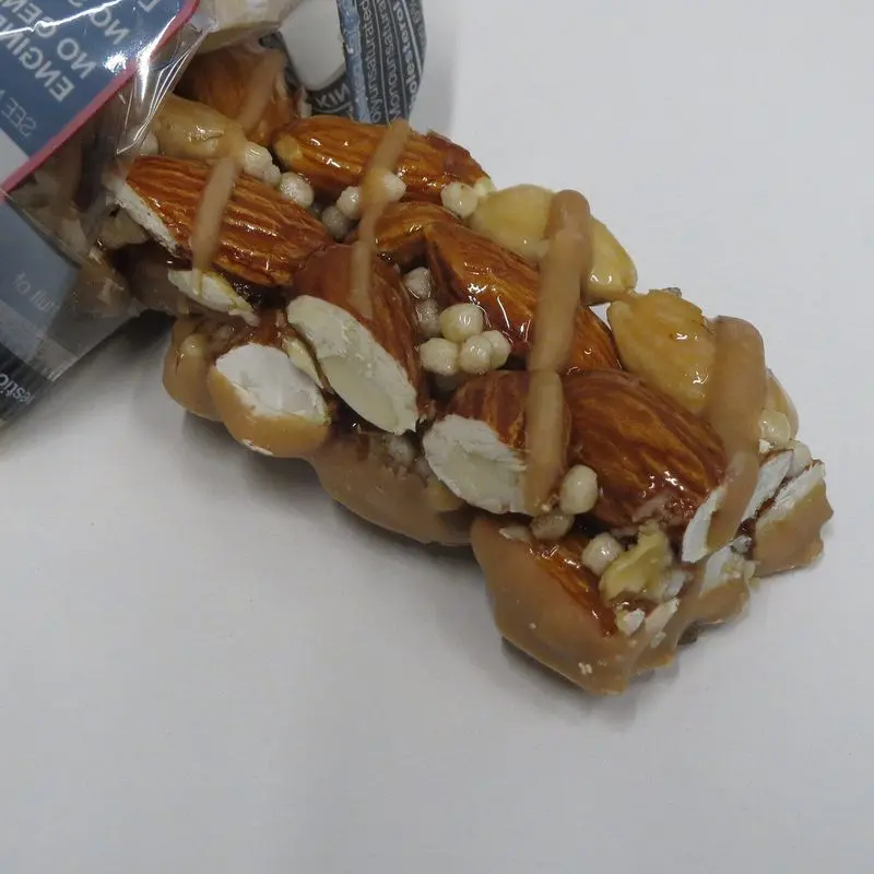 Barrita de cereales con almendras enteras y caramelo asomando de su envoltorio sobre fondo blanco