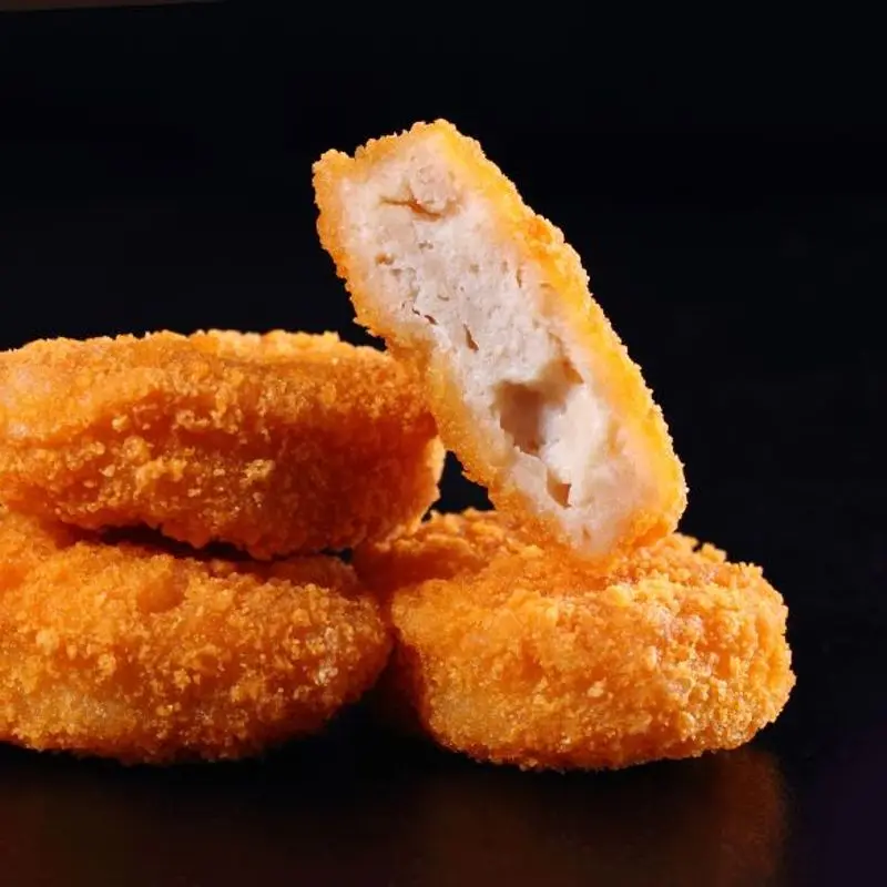 Nuggets de pollo empanados y dorados, uno abierto, sobre fondo negro