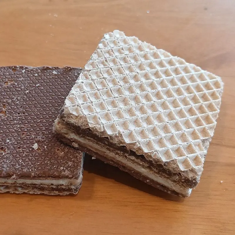 Dos barquillos rectangulares de oblea, uno de chocolate y otro de vainilla, sobre una mesa de madera