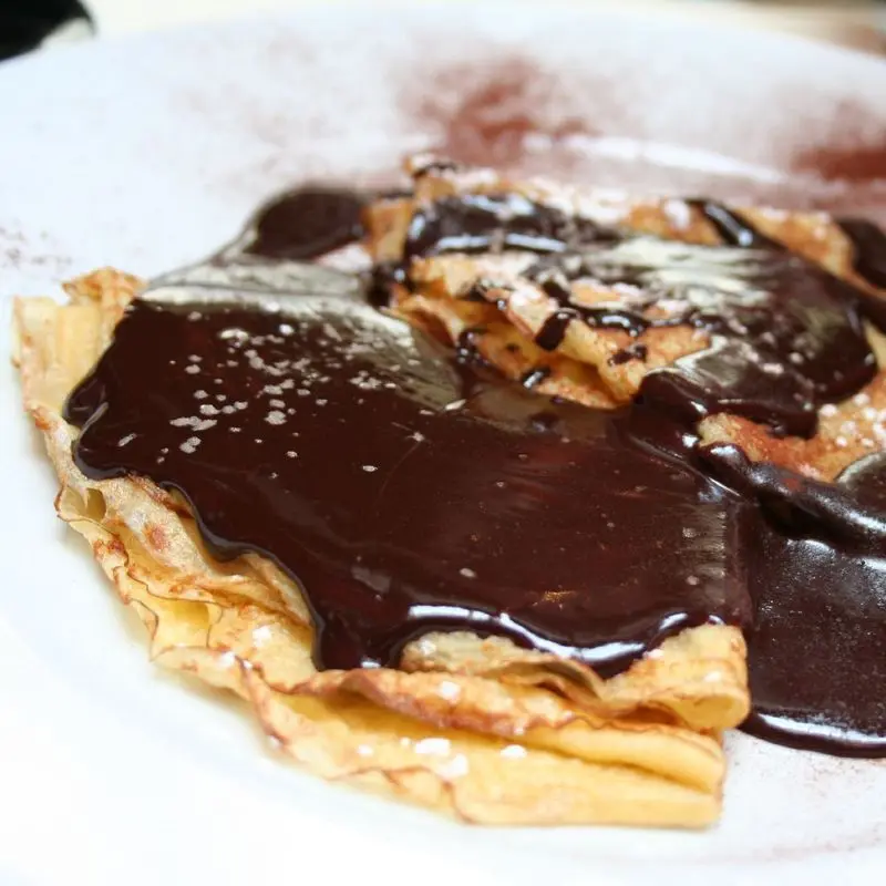 Crepes doblados cubiertos de salsa de chocolate en un plato blanco