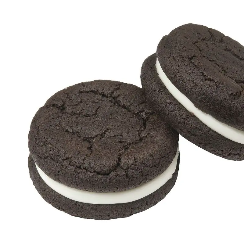 Dos galletas negras de cacao rellenas de crema blanca sobre fondo blanco