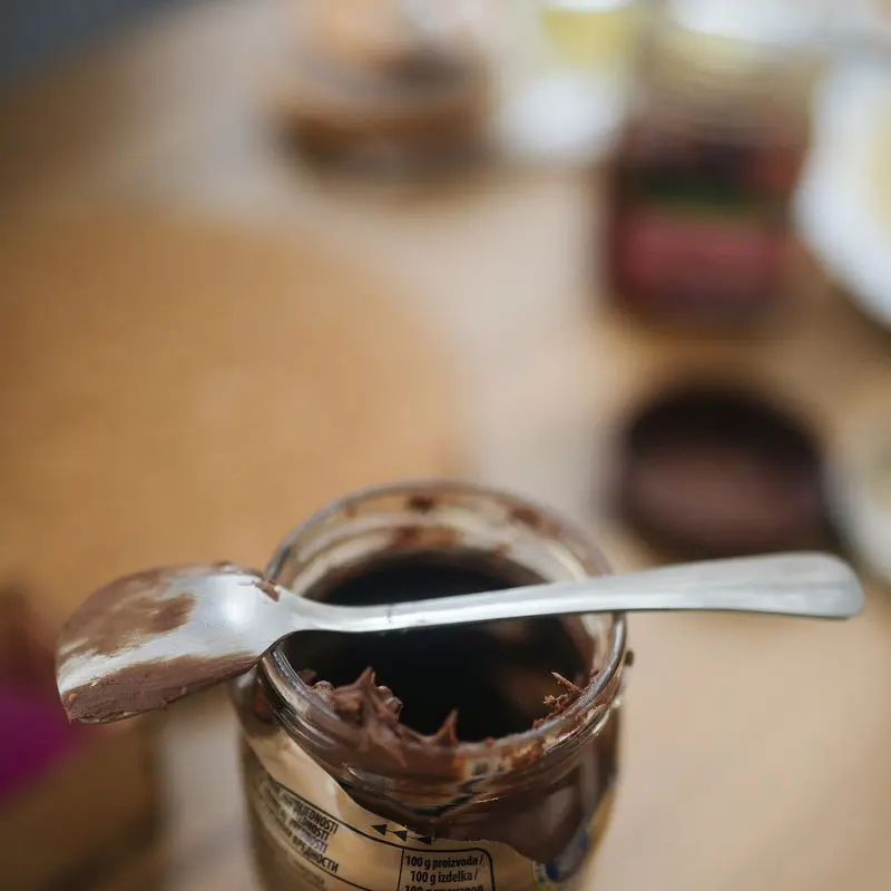 Tarro de cristal con crema de cacao y avellanas y una cuchara apoyada