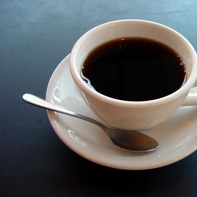 Taza blanca de café negro con cucharilla sobre un plato