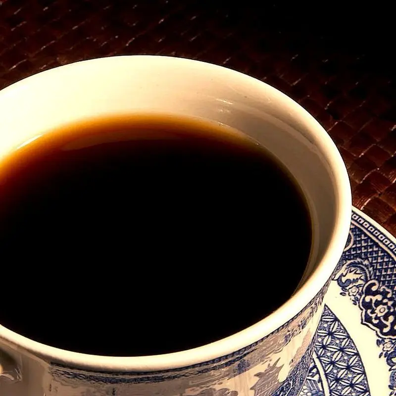 Taza de café negro vista desde arriba sobre un plato de cerámica decorado
