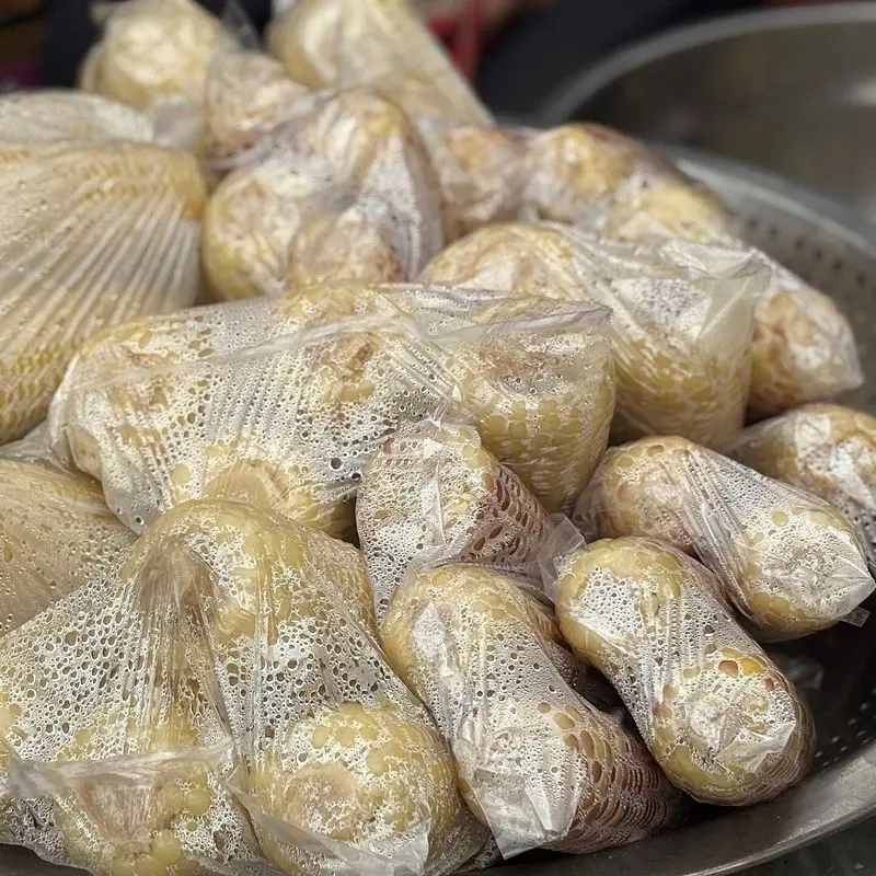 Mazorcas de maíz cocidas envueltas individualmente en plástico, amontonadas en una bandeja