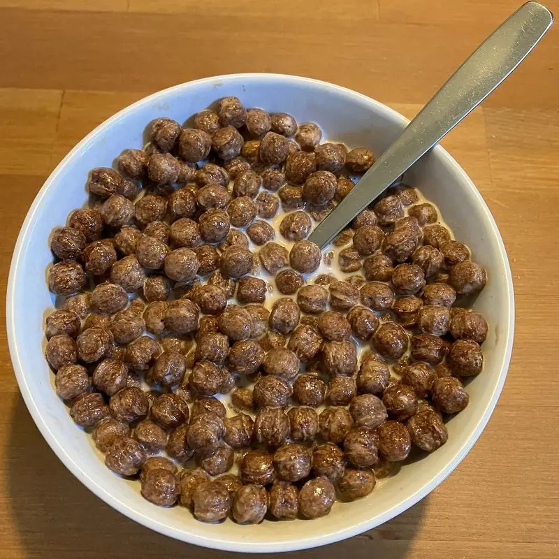 Cuenco blanco de bolitas de cereal de chocolate con leche y una cuchara
