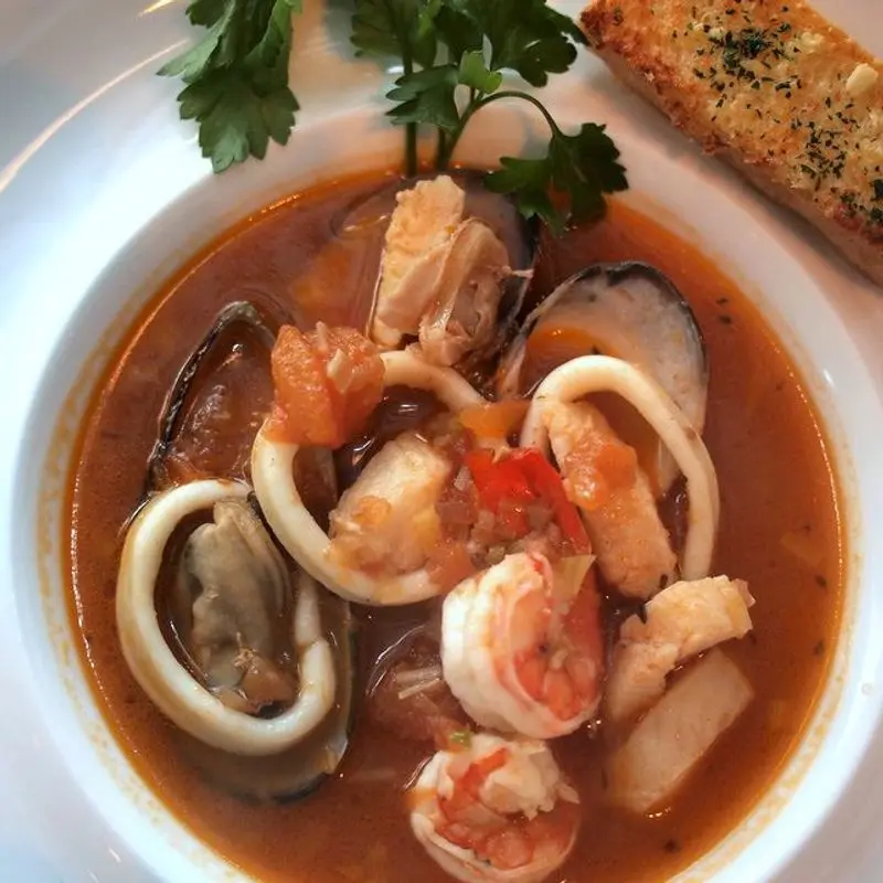 Plato de sopa de pescado y marisco con mejillones, calamares y gambas en caldo rojizo