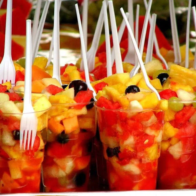 Vasitos de plástico con macedonia de frutas troceadas de colores y tenedores