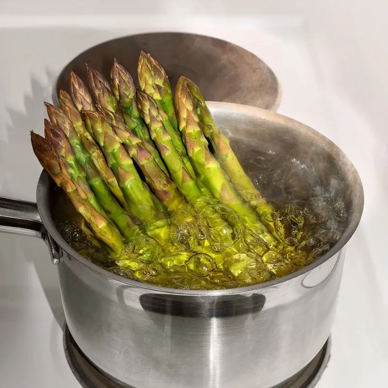 Espárragos verdes cocidos asomando de una olla de acero inoxidable