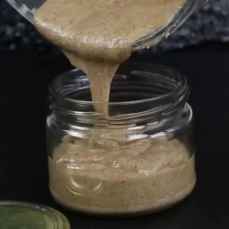 Crema de avellanas casera cayendo en un tarro de cristal sobre fondo oscuro