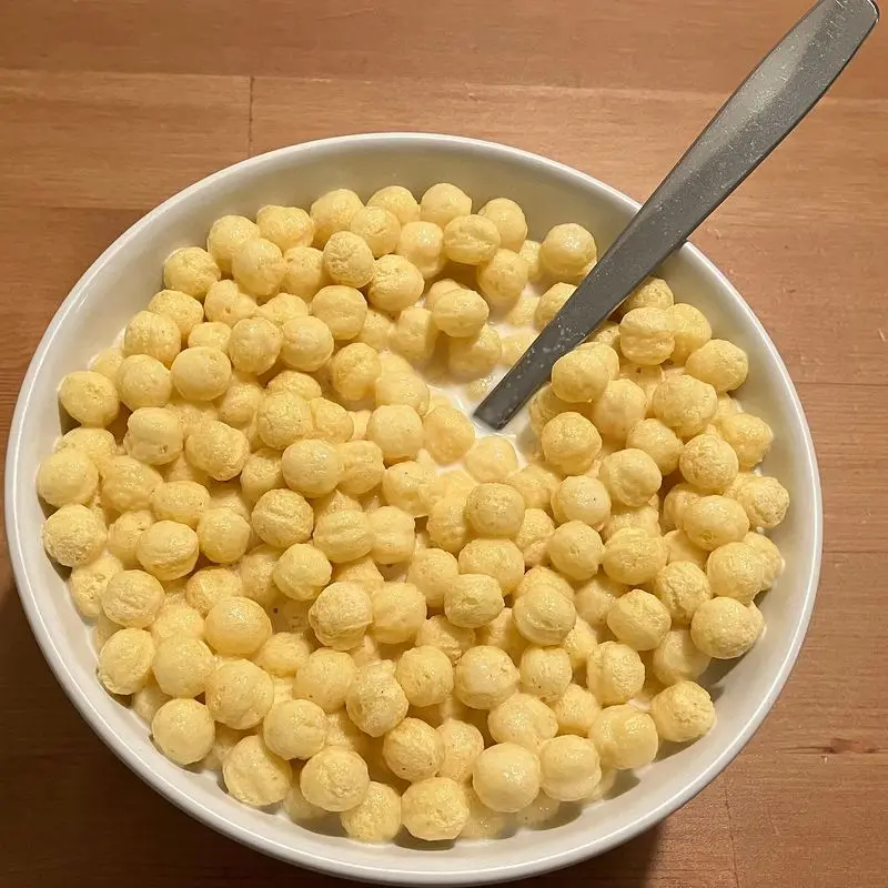 Cuenco blanco de bolitas de maíz doradas con leche y una cuchara
