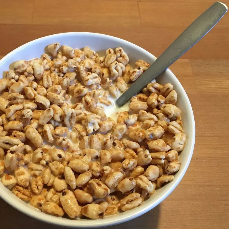 Cuenco blanco de trigo inflado con miel, con leche y una cuchara