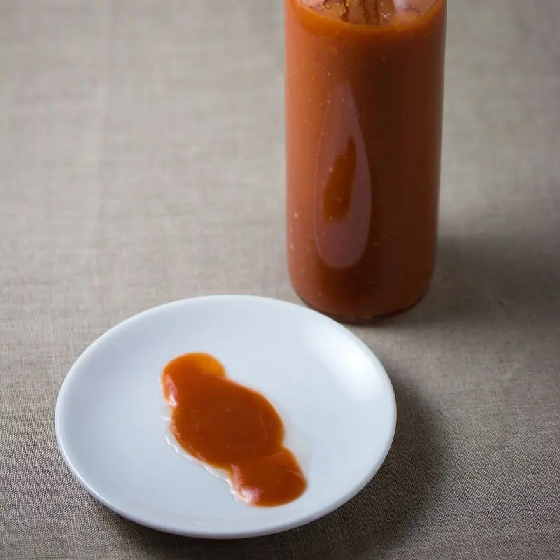 Botella de cristal de salsa picante roja sin etiqueta junto a un plato
