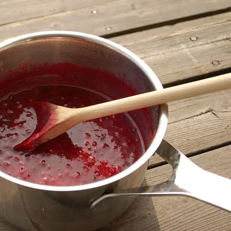 Cazo de acero con mermelada roja de frutos del bosque y cuchara de madera