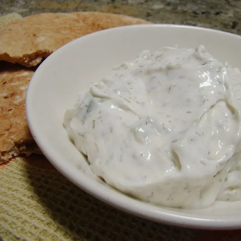 Cuenco blanco de salsa cremosa de yogur y ajo con pan al fondo