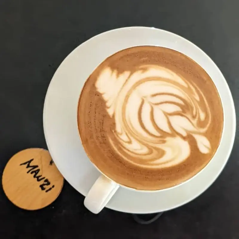 Taza de café con leche vista desde arriba con espuma dibujada sobre un plato blanco