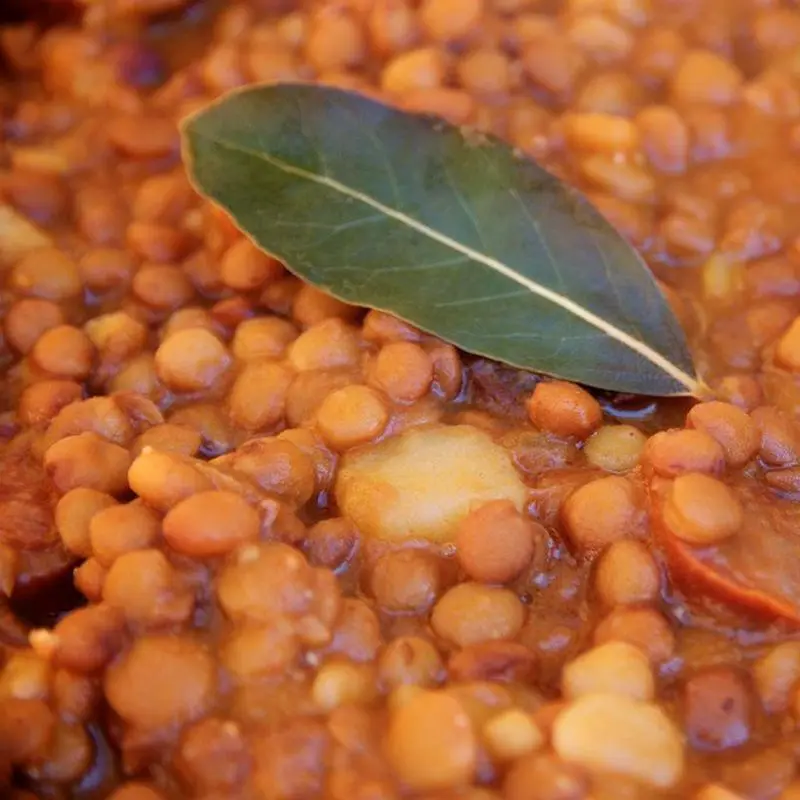 Lentejas guisadas con rodajas de chorizo y una hoja de laurel en primer plano
