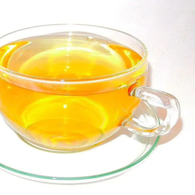 Taza de cristal con platillo transparente llena de una infusión dorada