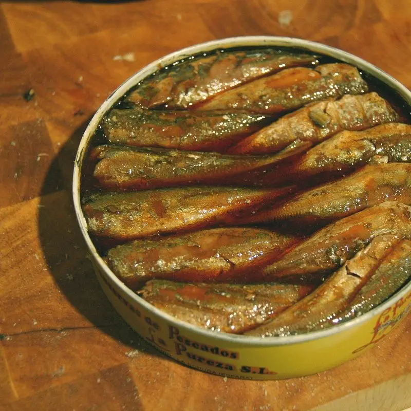 Lata abierta de pescado en escabeche con los lomos dorados sobre una tabla de madera