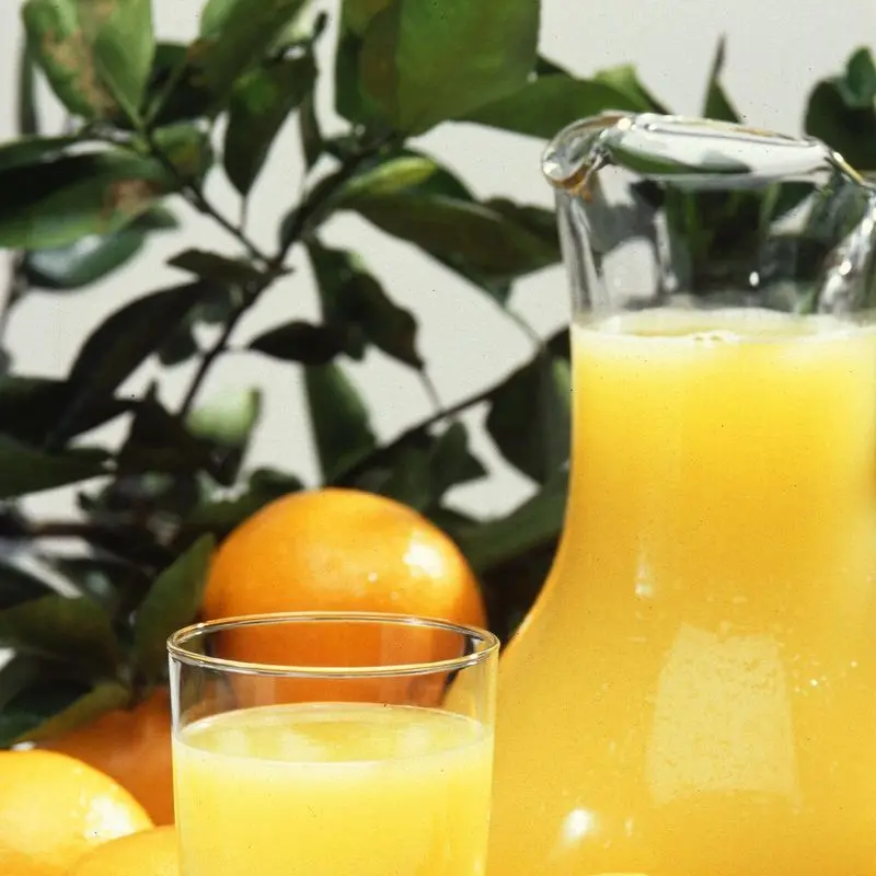 Vaso y jarra de zumo de cítricos anaranjado junto a naranjas frescas