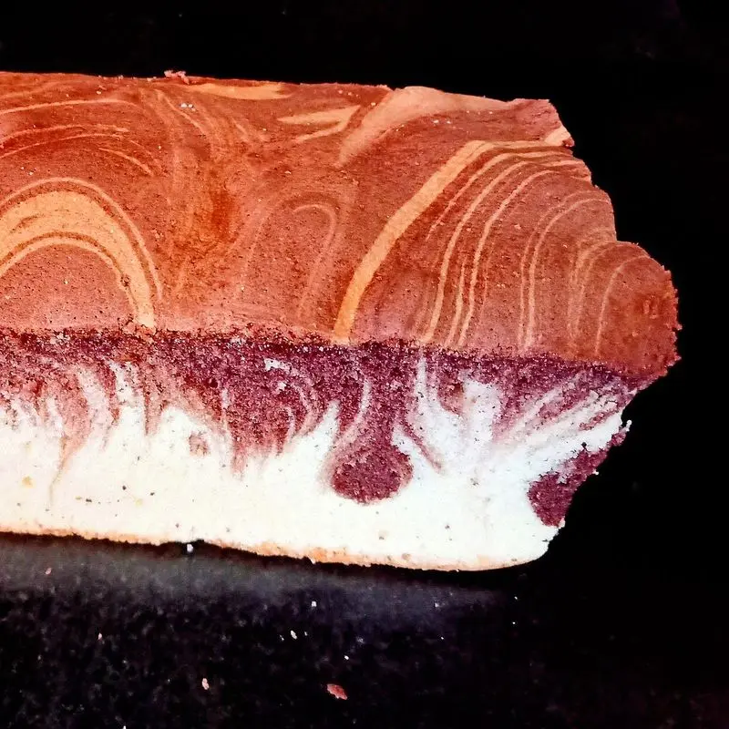 Trozo de bizcocho marmolado con vetas de chocolate y vainilla sobre fondo oscuro