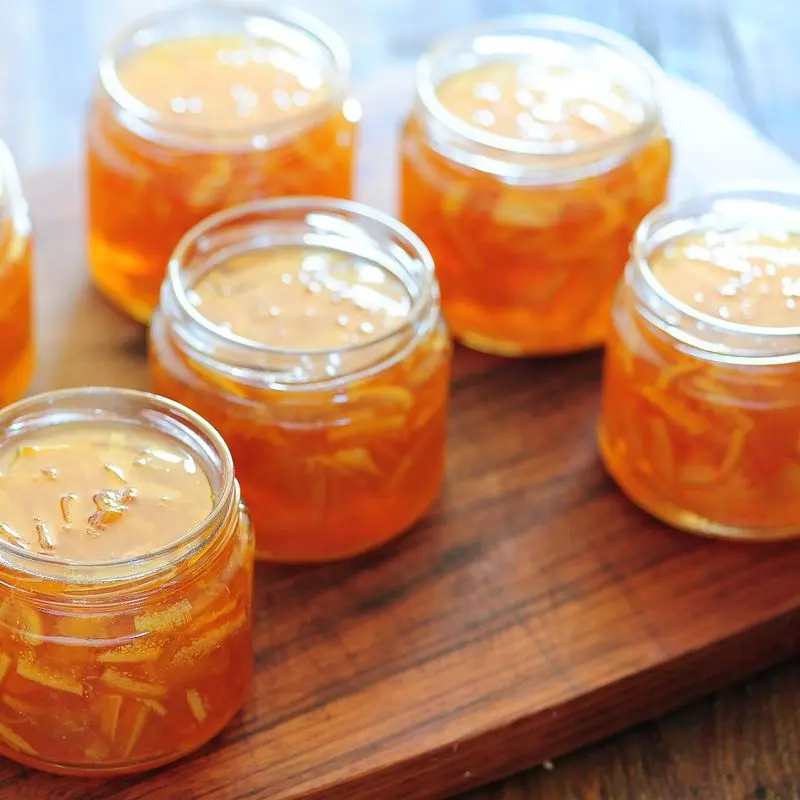 Tarros pequeños de mermelada de naranja con tiras de cáscara sobre una tabla de madera