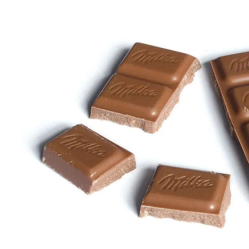 Tableta de chocolate con leche partida en trozos sobre fondo blanco