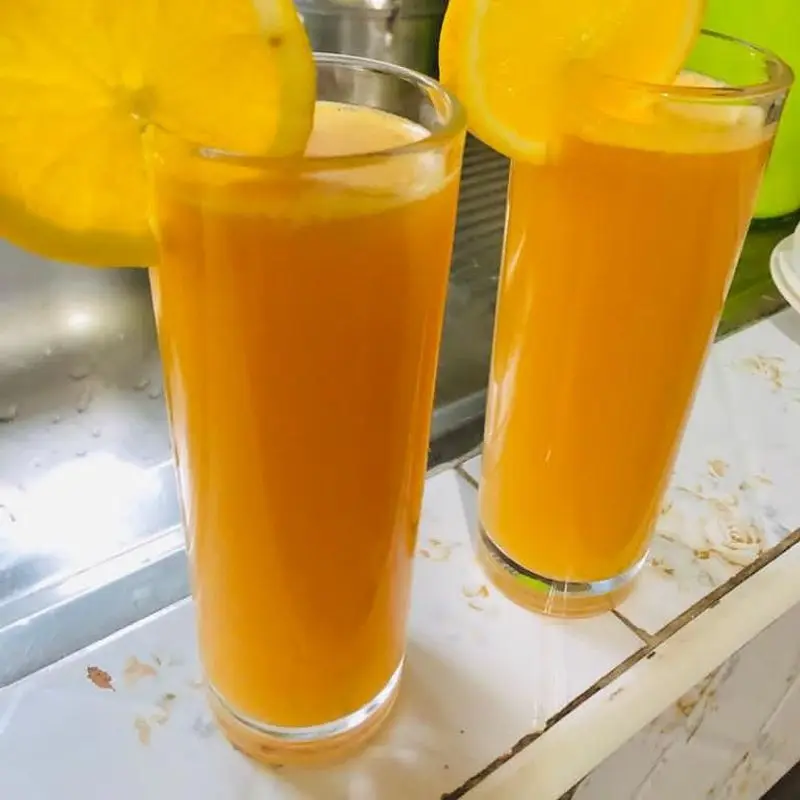 Dos vasos de zumo de fruta anaranjado con rodajas de limón sobre una mesa