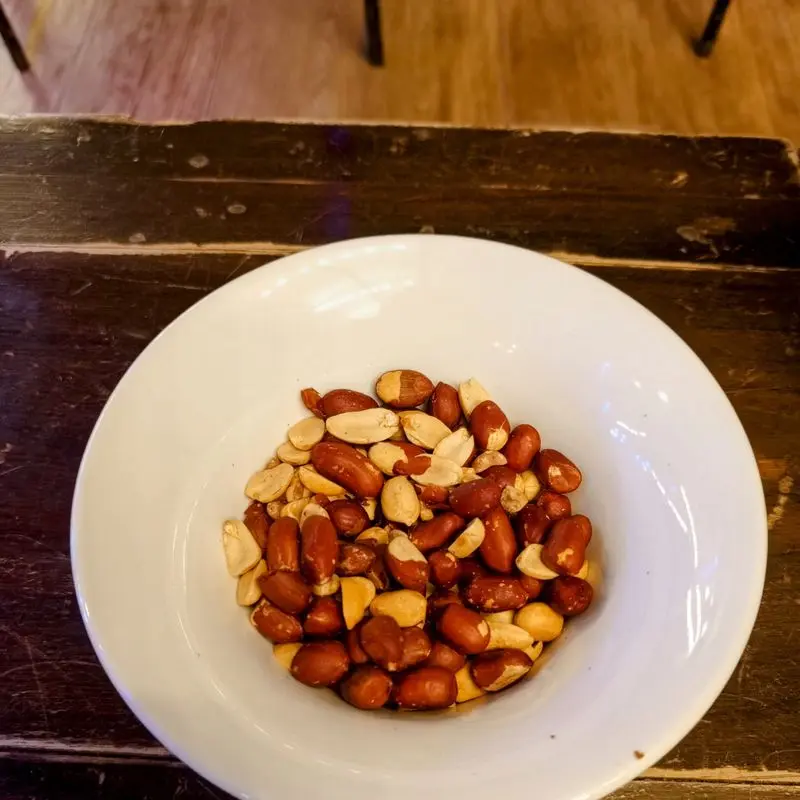 Cuenco blanco con cacahuetes tostados y salados sobre una mesa de madera oscura