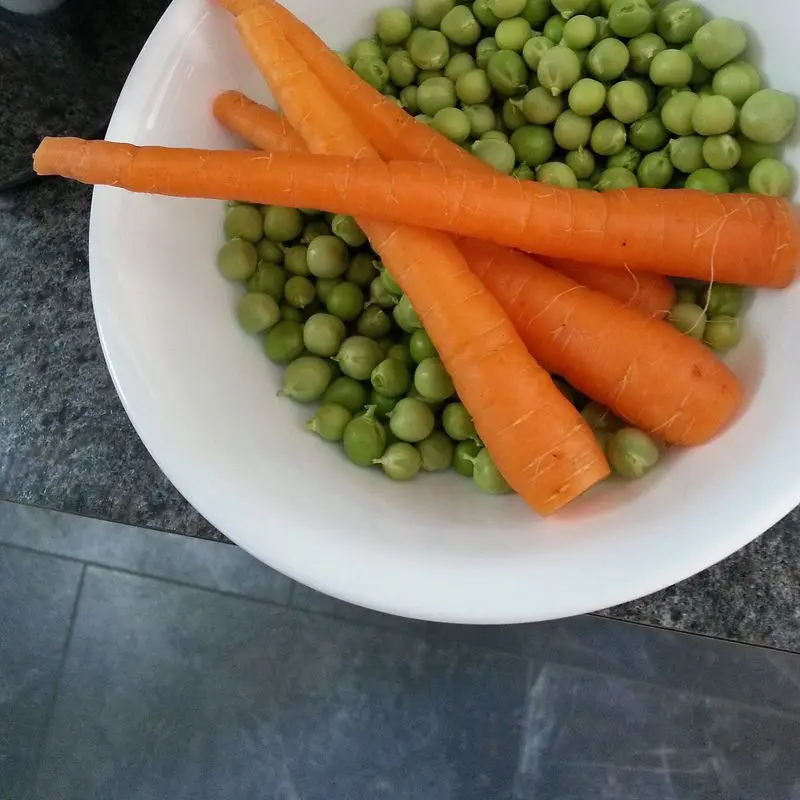 Guisantes verdes y zanahorias en un cuenco blanco