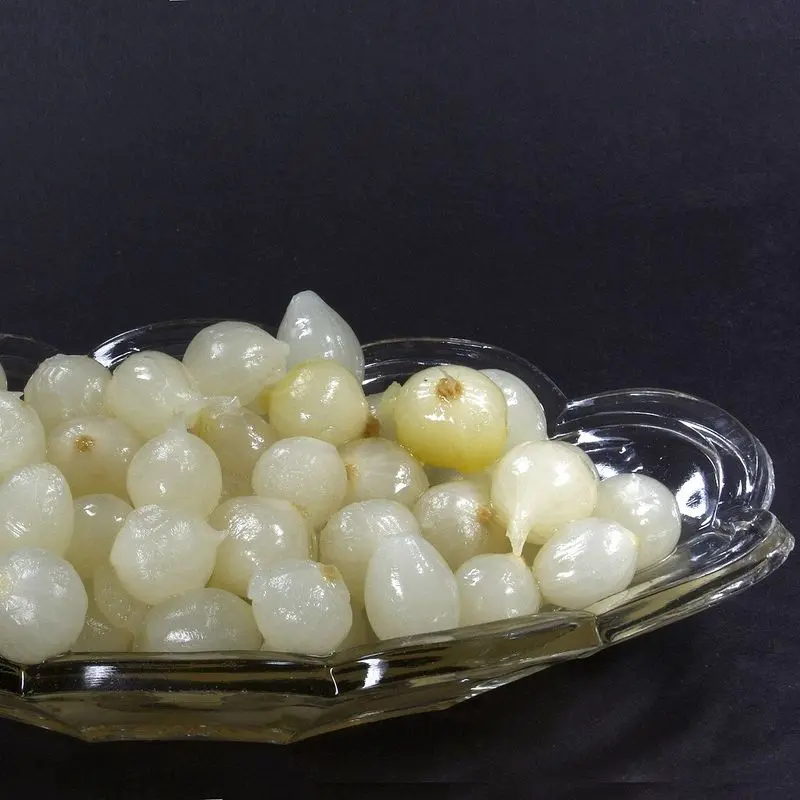 Cebollitas pequeñas en vinagre en un plato de cristal sobre fondo oscuro