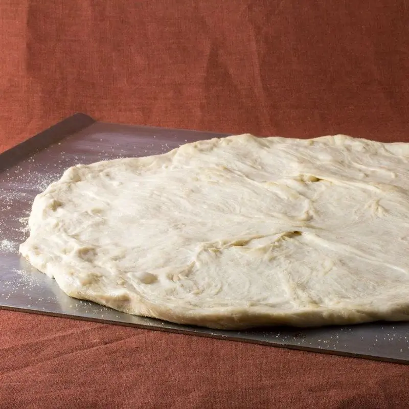 Base de pizza redonda sin ingredientes sobre una bandeja de horno