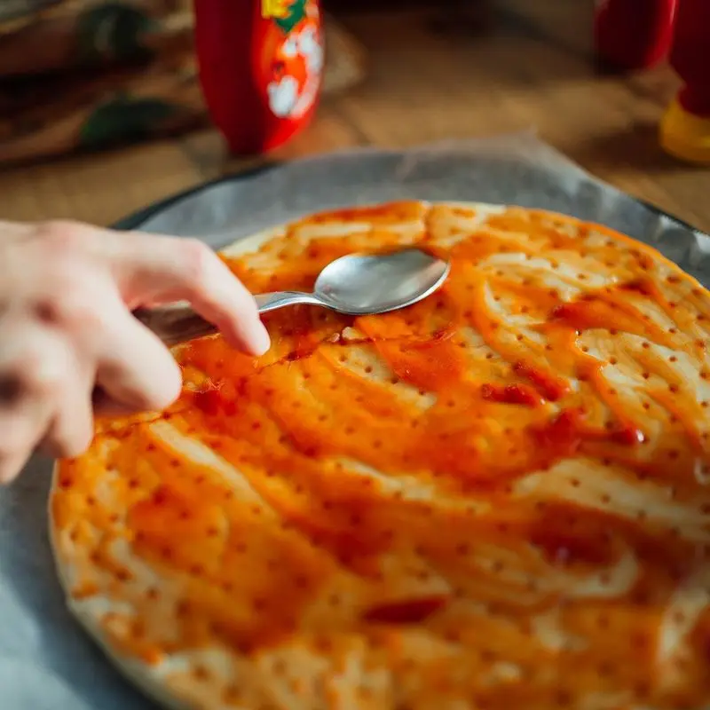 Masa de pizza cubierta con salsa de tomate extendida con una cuchara