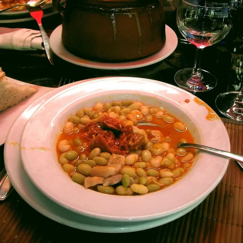 Plato hondo de pochas cocidas en salsa con chorizo, sobre una mesa