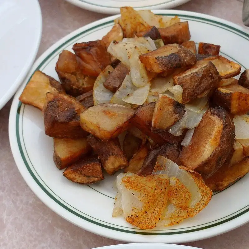 Patatas en dados fritas y doradas con cebolla en un plato blanco de borde verde