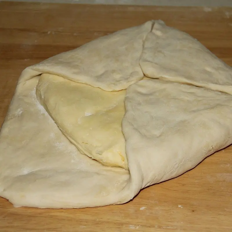 Masa de hojaldre plegada envolviendo una lámina de mantequilla sobre tabla de madera