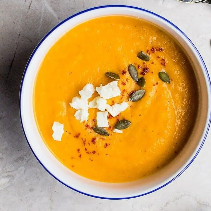 Cuenco de crema de calabaza naranja con pipas y trocitos de queso