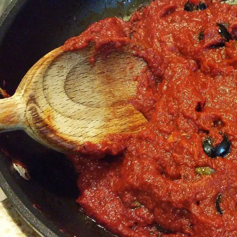 Salsa de tomate espesa con aceitunas negras en una sartén con cuchara de madera