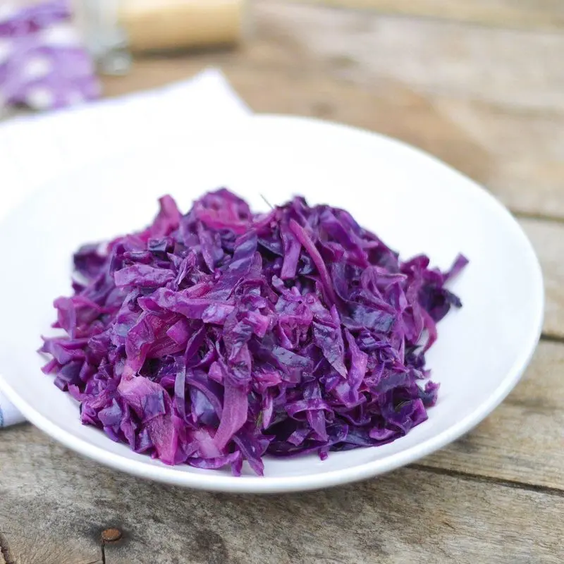 Plato blanco con lombarda cocida de color morado intenso sobre una mesa de madera