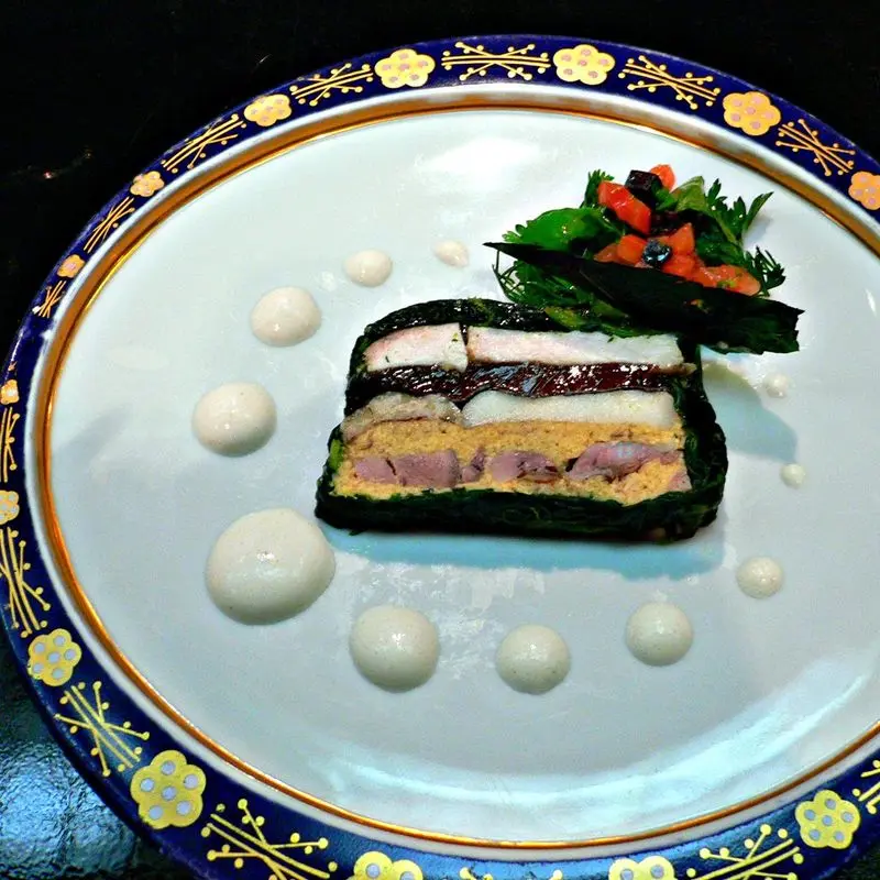 Porción de pastel de marisco en capas servida sobre un plato blanco con adorno de hierbas